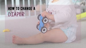 baby in diaper sits on the ground holding a toy car