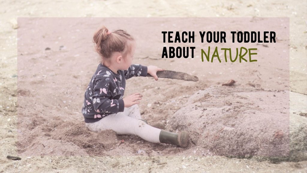 toddler girl sits in the sand playing with a stick and boulder