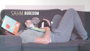 bored stay-at-home mom lays on the sofa with baby books and stuffed animals